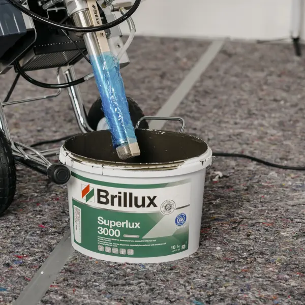 Brillux-Farbeimer Superlux 3000 mit angeschlossenem Malergerät auf einer Schutzmatte