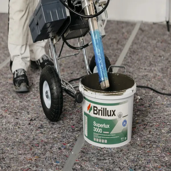 Brillux-Farbeimer Superlux 3000 mit angeschlossenem Malergerät auf einer Schutzmatte