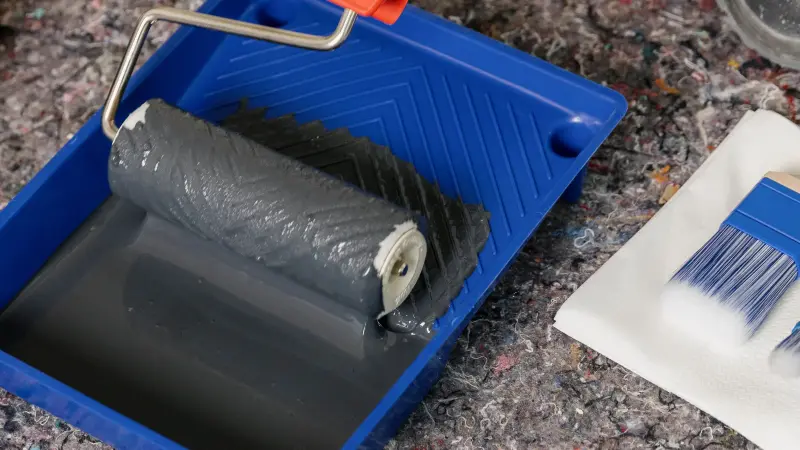 Blaue Farbwanne mit grauer Farbe darin und einer Rolle.