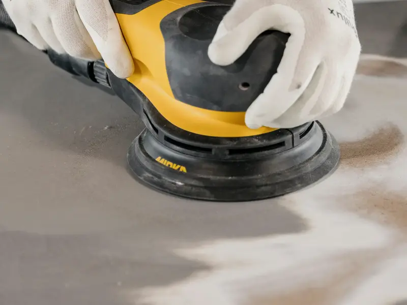 Eine Person schleift mit einem Mirka Schleifgerät einen Tisch ab