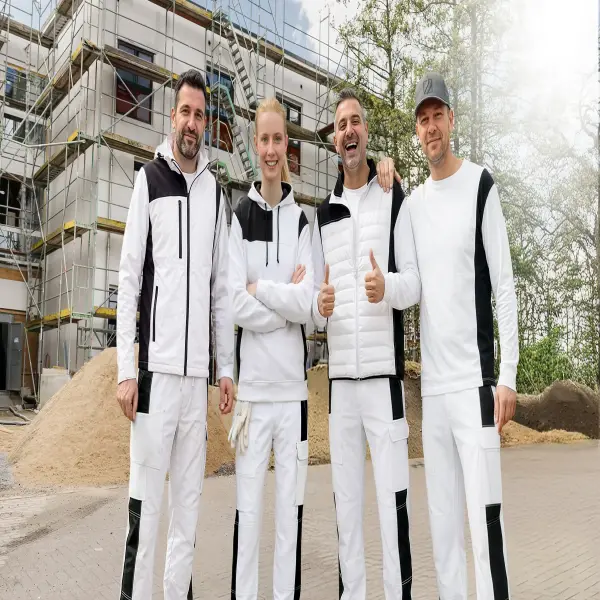 Maler und eine Malerin stehen vor einer Baustelle. Alle tragen moderne und professionelle Berufsbekleidung.