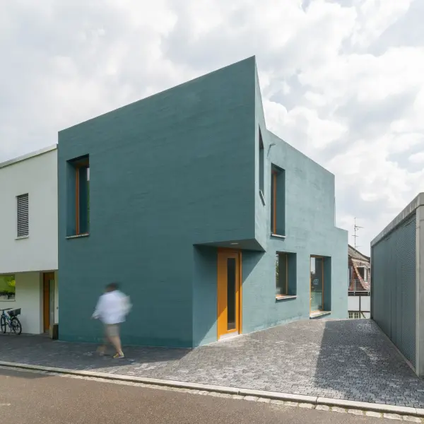 Eckiges Haus mit türkisener Fassade und brauner Holztür