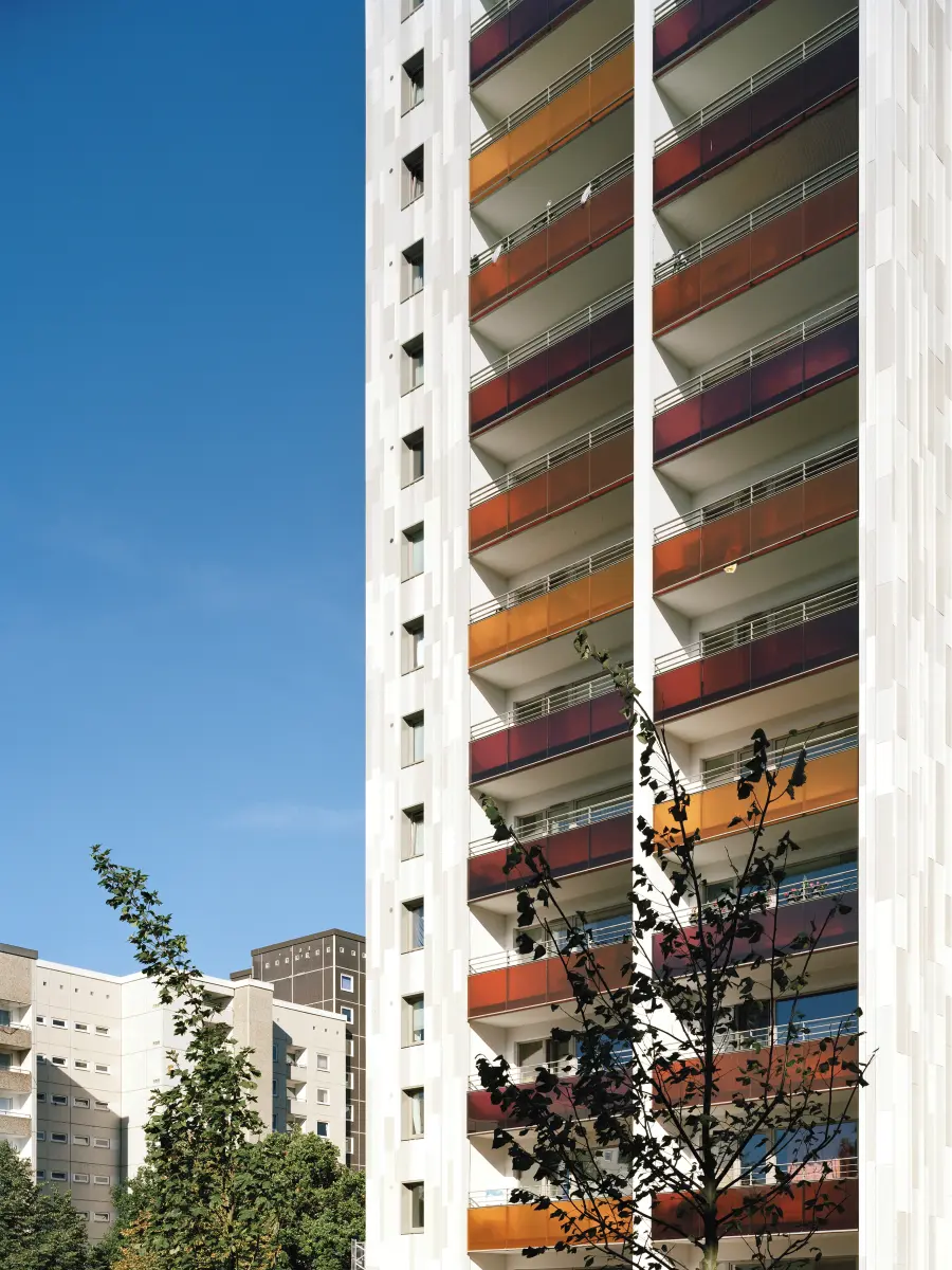 Hochhausfassade mit farbigen Balkonen in Gelb‑ und Rottönen vor blauem Himmel.