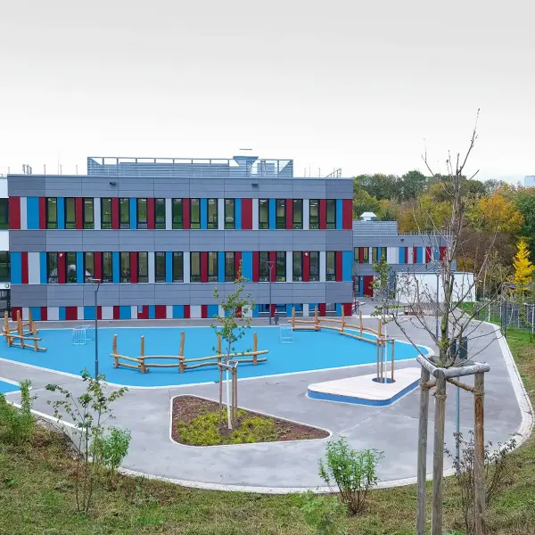 Sportzentrum Gebäude in blau, weiß, rot und grau mit blauem Sportplatz davor