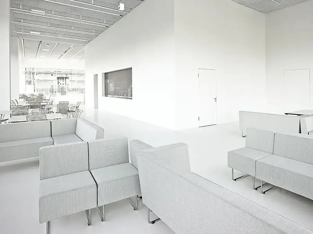 Helles, modern gestaltetes Interieur mit minimalistischen, grauen Sofas, weißen Wänden und großen Fenstern im Hintergrund.