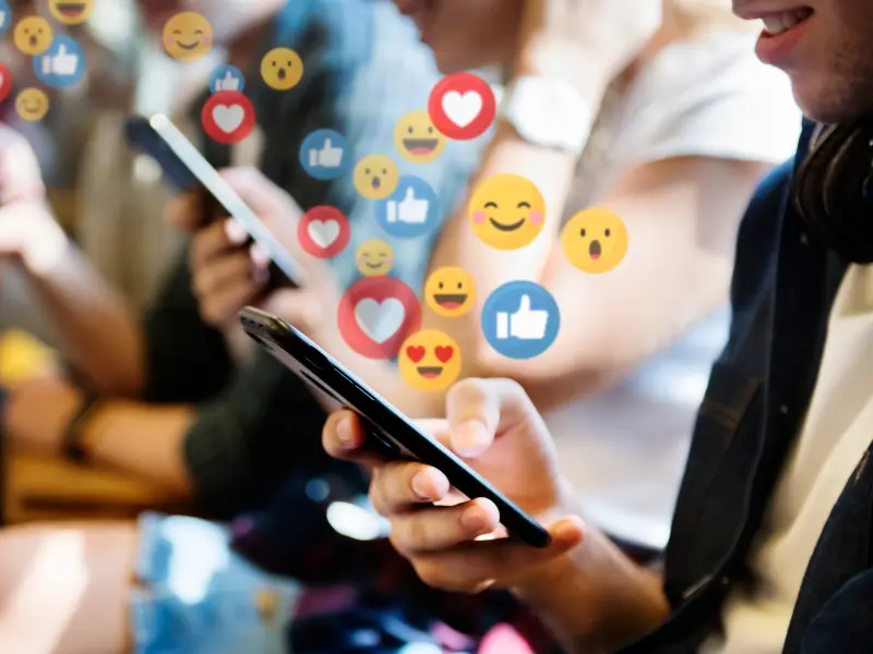 Eine Person schaut auf ihr Handy. Viele Emojis fliegen darüber