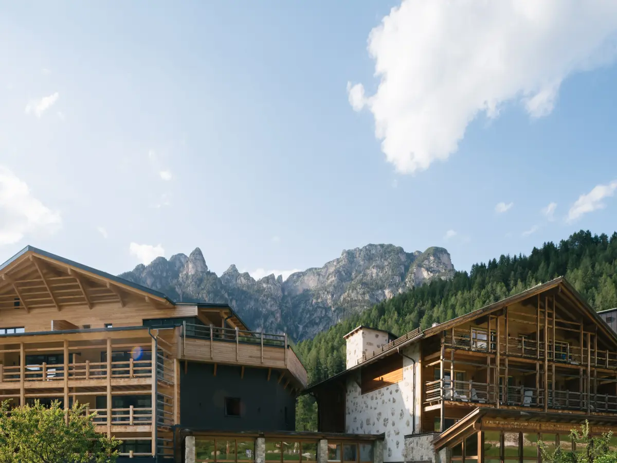 Facciata in legno di un hotel nelle Alpi con cielo azzurro e montagna sullo sfondo.