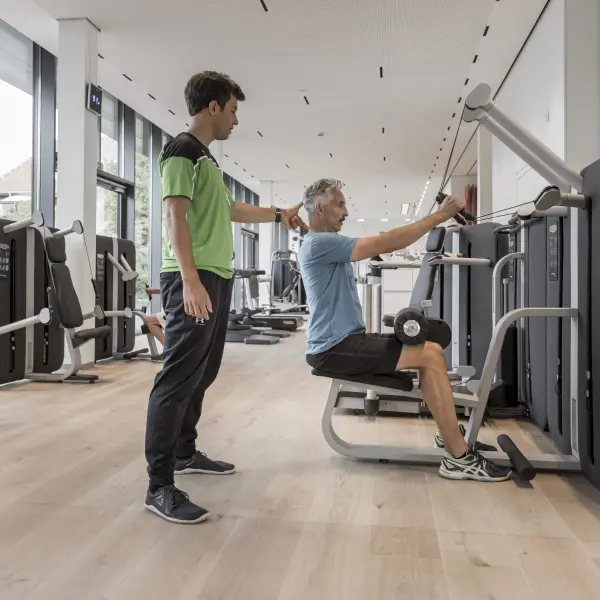 Zwei Personen im Fitnessstudio stehen an einem Fitnessgerät
