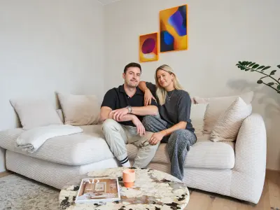 Philipp und Sara sitzen auf einem hellen Sofa und schauen in die Kamera