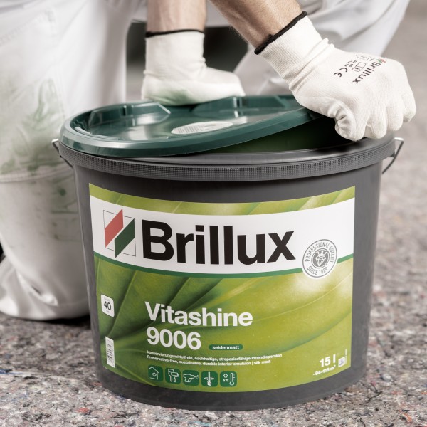  Ein Maler mit weißen Handschuhen öffnet einen großen, dunkelgrauen Eimer Brillux Vitashine 9006 Wandfarbe.