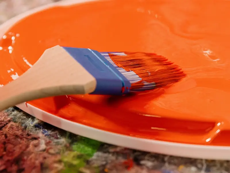 Farbe in Orange auf einem Deckel mit einem Pinsel, die in die Farbe getunkt wird.