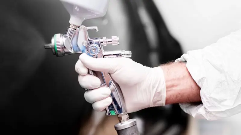 Farbpistole sprüht auf schwarzes Auto