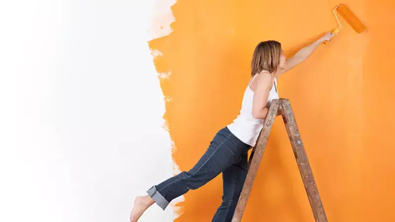 Frau steht auf einer Leiter und streicht