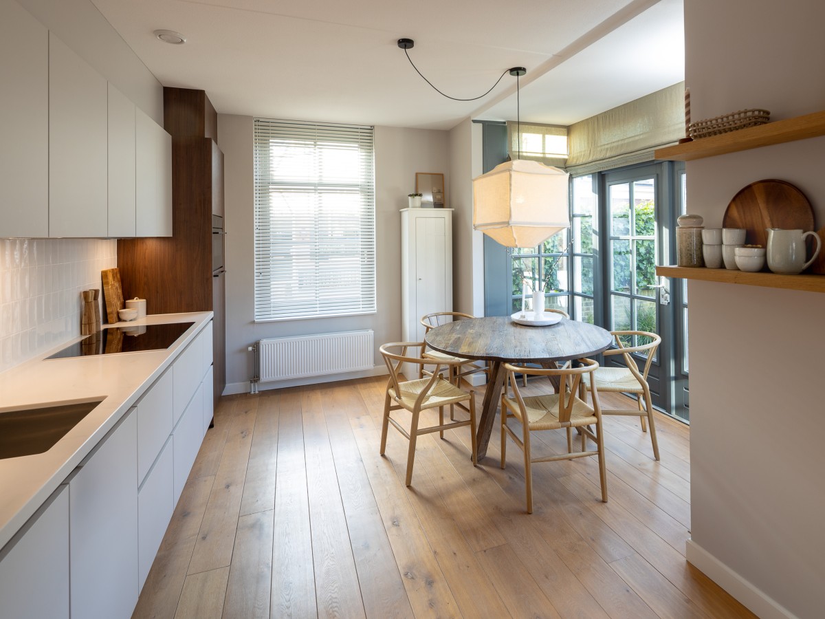 Eine moderne Küche mit weißen Schränken, einem runden Holztisch mit vier Stühlen und Holzboden.