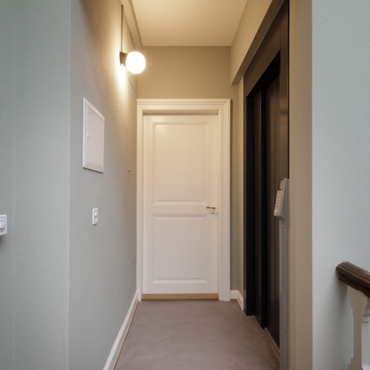 Heller Hotelflur mit Aufzug, weißer Tür und Wandlampe.