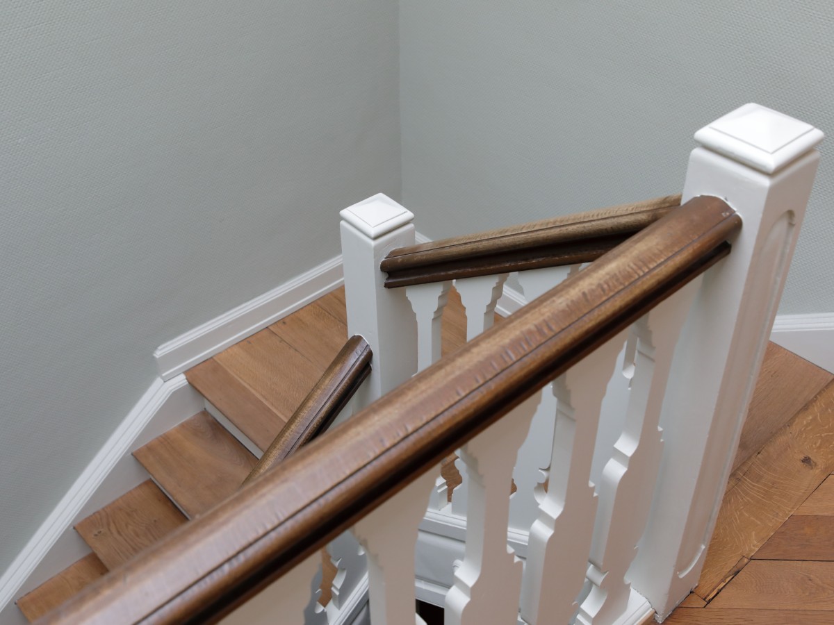 Holztreppe mit weißem Geländer und braunem Handlauf in einem hellen Treppenhaus.