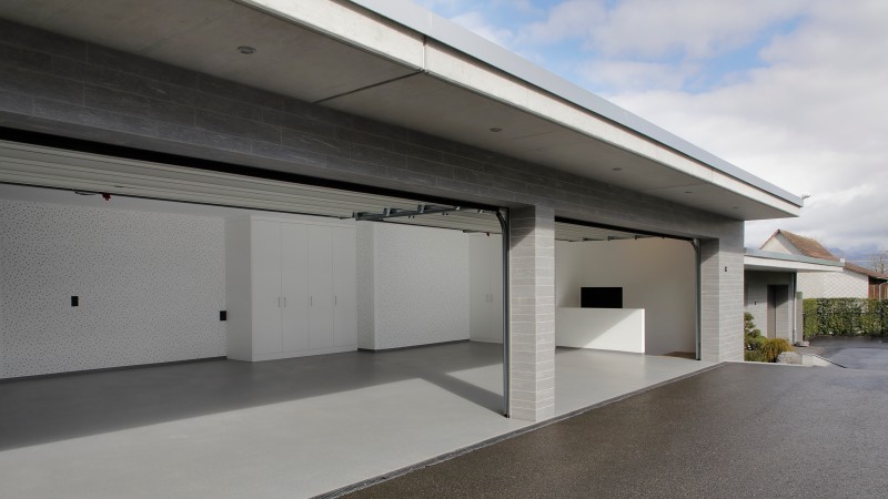 Moderne Doppelgarage mit geöffneten Toren, weißen Einbauschränken und grauem Boden.