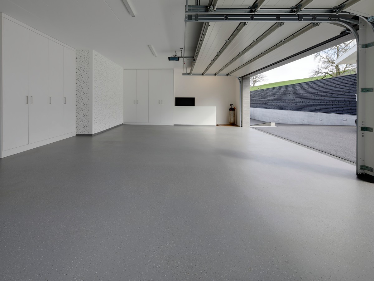 Große moderne Garage mit offenem Tor, weißen Einbauschränken und grauem Boden.