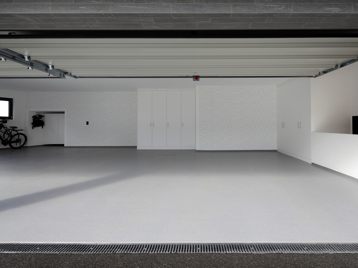 Große, moderne Garage mit offenem Tor, weißen Einbauschränken und grauem Boden.