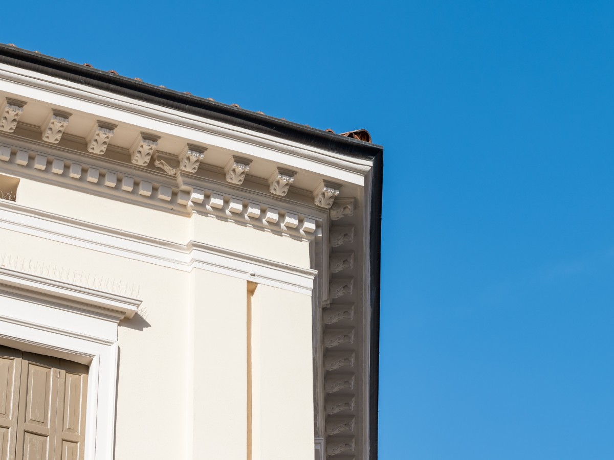 Eine Nahaufnahme eines historischen Gebäudes mit Gesims und Verzierungen unter klarem blauem Himmel.