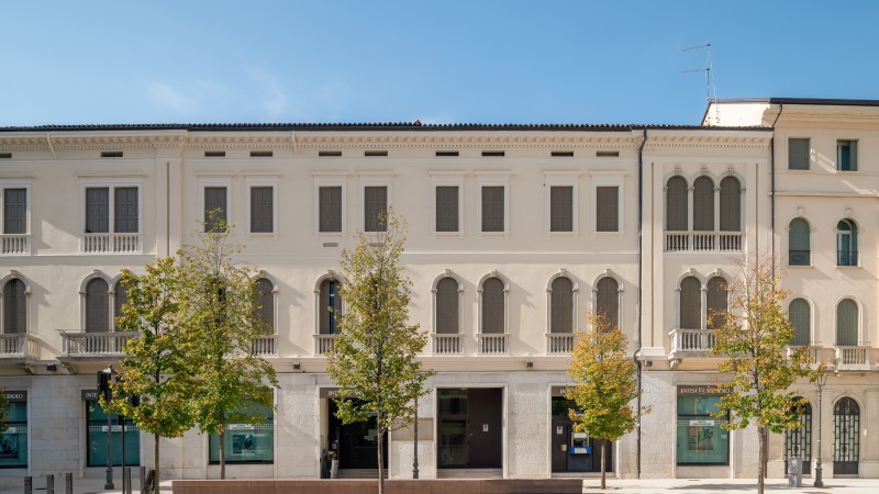 Ein langes, historisches italienisches Gebäude mit vielen Fenstern und Bäumen davor, fotografiert an einem sonnigen Tag.