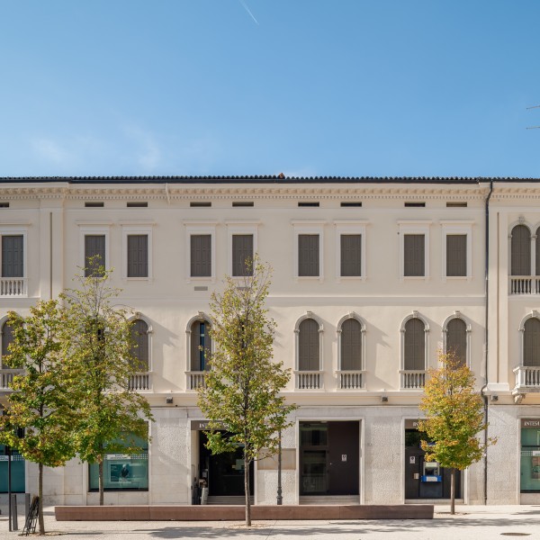 Ein langes, historisches italienisches Gebäude mit vielen Fenstern und Bäumen davor, fotografiert an einem sonnigen Tag.