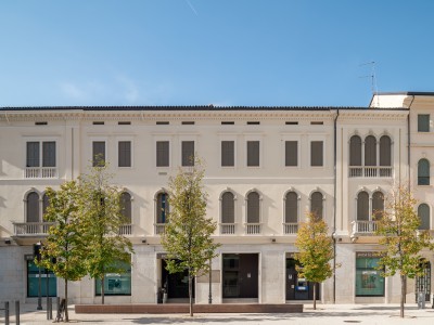 Ein langes, historisches italienisches Gebäude mit vielen Fenstern und Bäumen davor, fotografiert an einem sonnigen Tag.