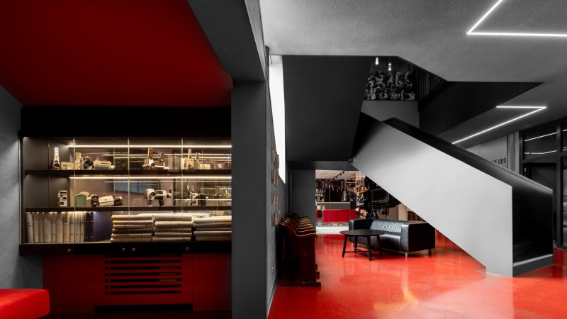Ein moderner Raum mit glänzend rotem Boden, einer schwarzen Treppe und einer beleuchteten Vitrine, die verschiedene Objekte zeigt.