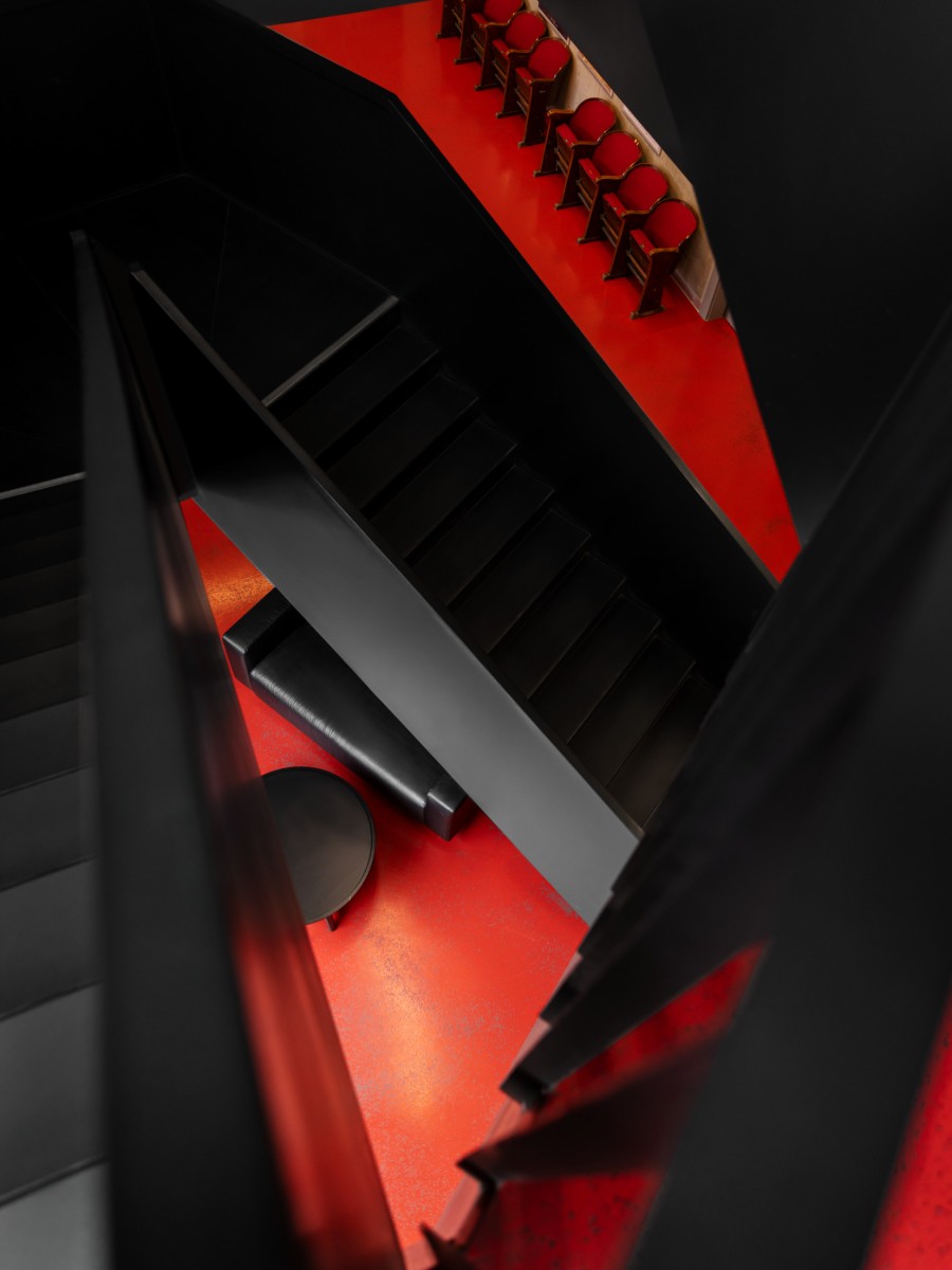 Eine abstrakte, von oben fotografierte Innenansicht einer modernen, schwarzen Treppe mit einem leuchtend roten Boden.
