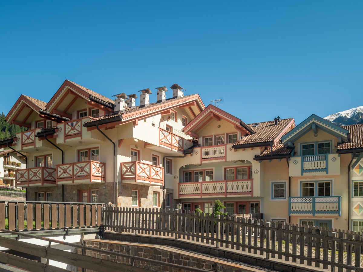 Ein großes, traditionelles Haus im Alpenstil mit Balkonen, Zäunen und einem schneebedeckten Berggipfel im Hintergrund.