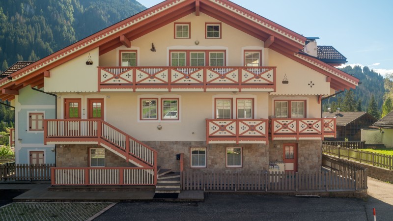 Ein traditionelles Haus im Alpenstil mit rotem Dach und Balkonen, mit Bergen im Hintergrund.