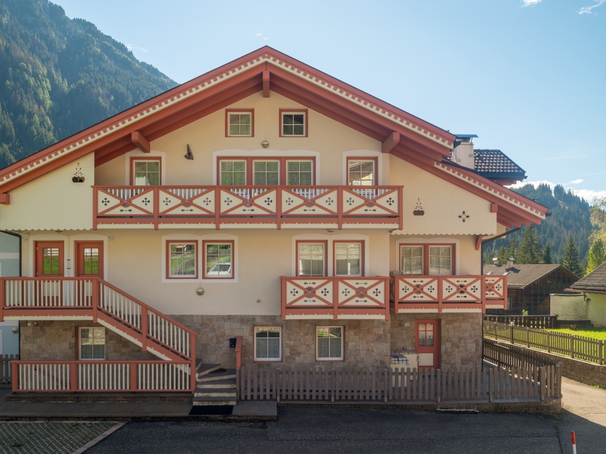 Ein traditionelles Haus im Alpenstil mit rotem Dach und Balkonen, mit Bergen im Hintergrund.