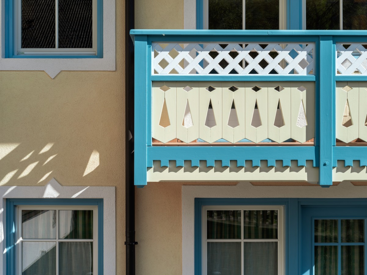 Eine Nahaufnahme eines Balkons und Fenstern eines traditionellen Hauses, mit blau-weißen Verzierungen und geschnitzten Holzgeländern.