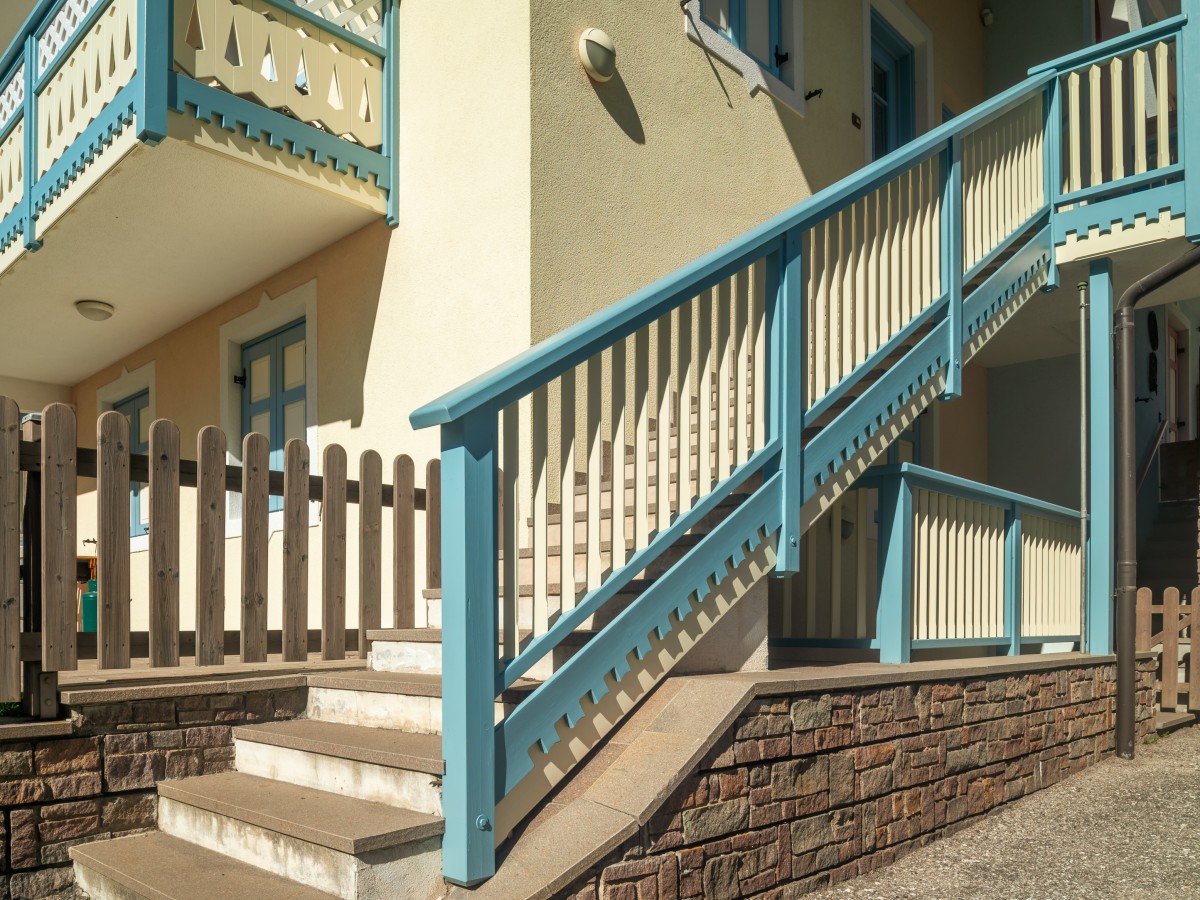 Eine Außentreppe aus Holz mit blau-weißem Geländer, die zu einem Balkon führt.