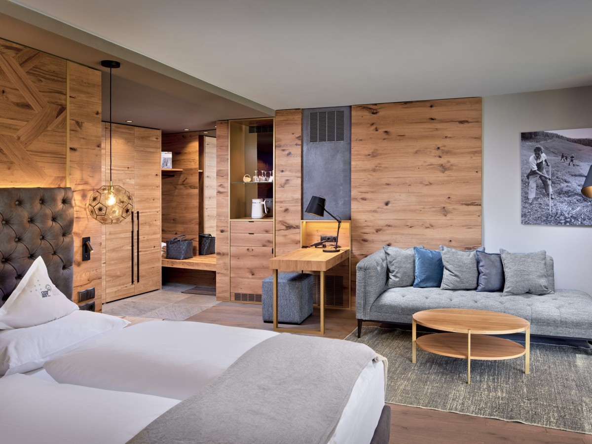 Hotelzimmer in Holzoptik mit weißem Bett und grauem Sofa