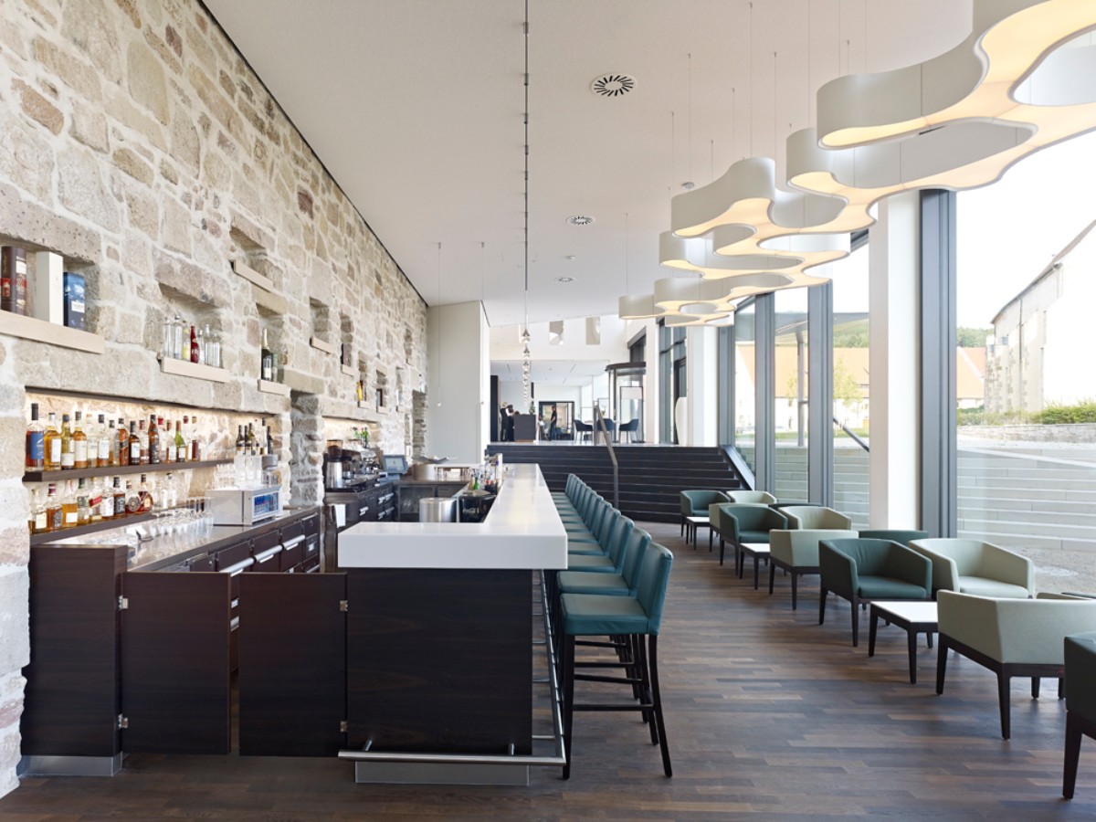 Eleganter Bar Bereich mit integrierter Klostermauer und Einrichtung geprägt von Grau-, Weiß- und Schwarztönen.