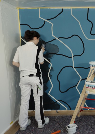 Türkisene Wand mit schwarzen Mustern und Maler davor