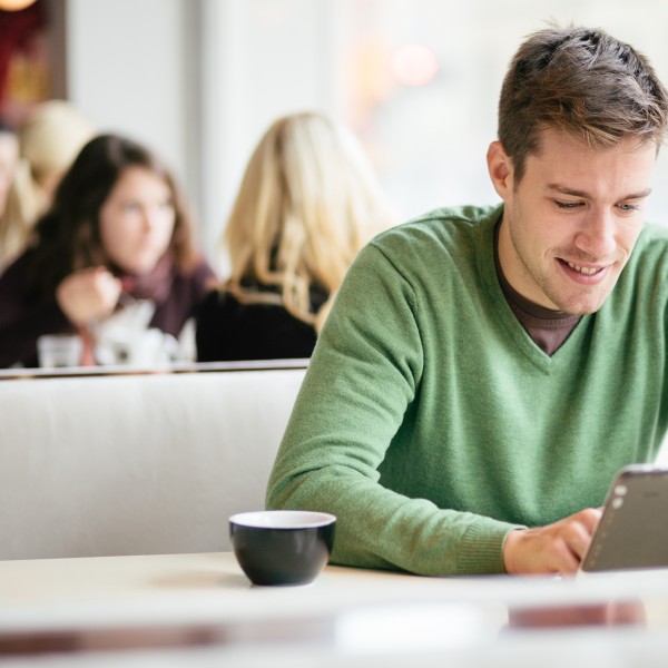 Mann mittleren Alters sitzt in einem Café und nutzt ein iPad, Hintergrund und andere Gäste unscharf